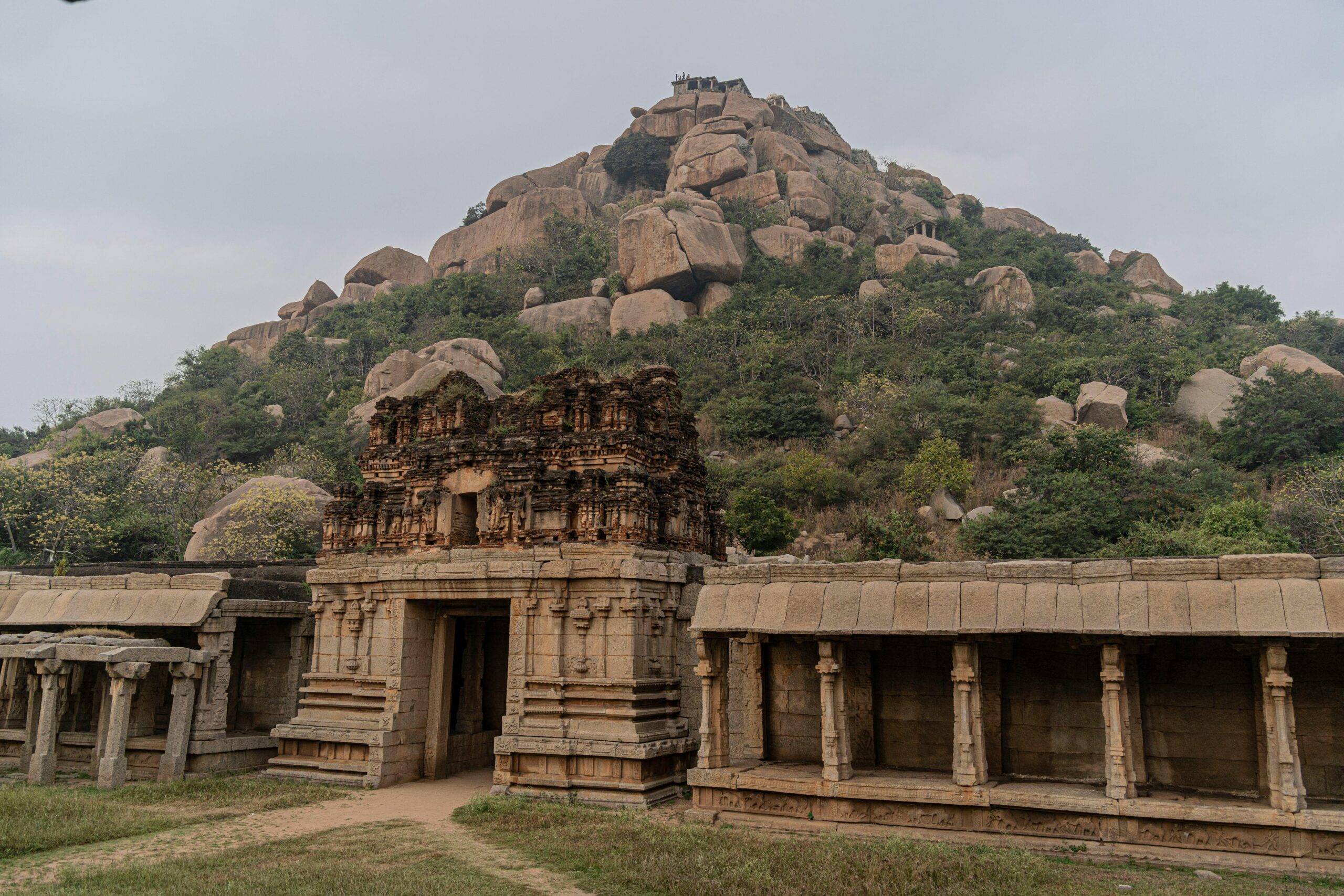 Explore the ancient stone temple ruins at Hampi, showcasing historic architecture against rocky hills.